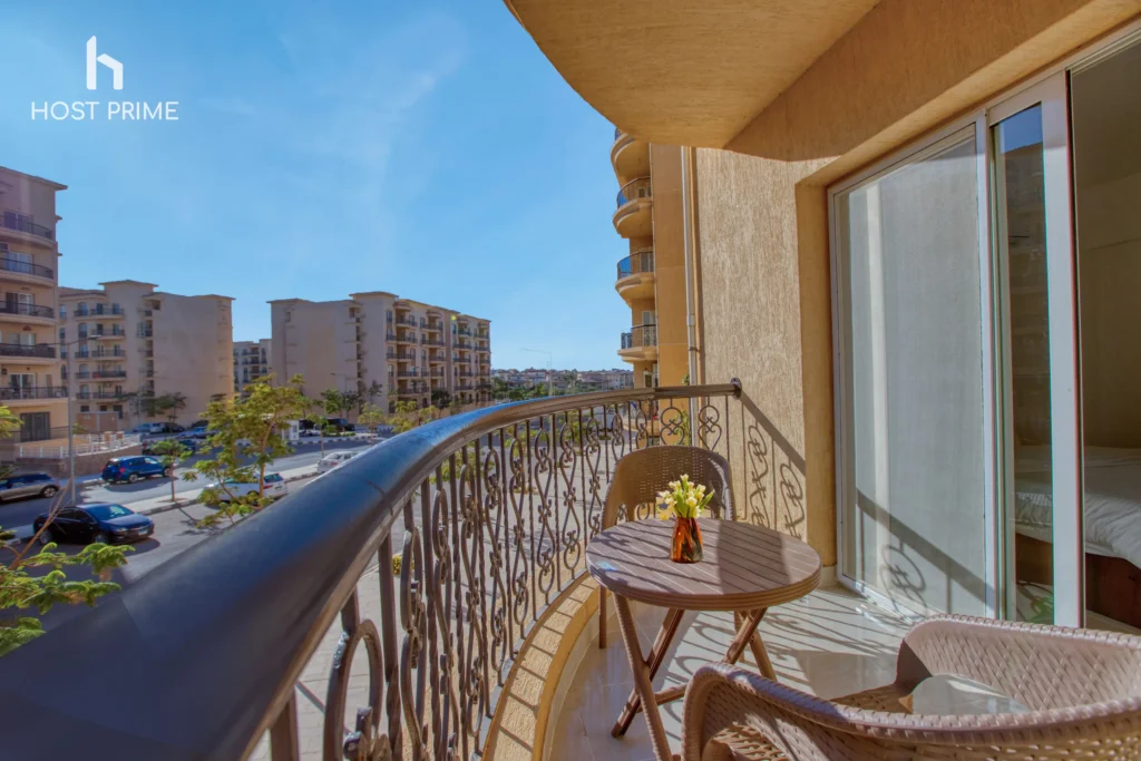 A balcony with a view of the city and a table with chairs in a 2-bedroom apartment in New Cairo