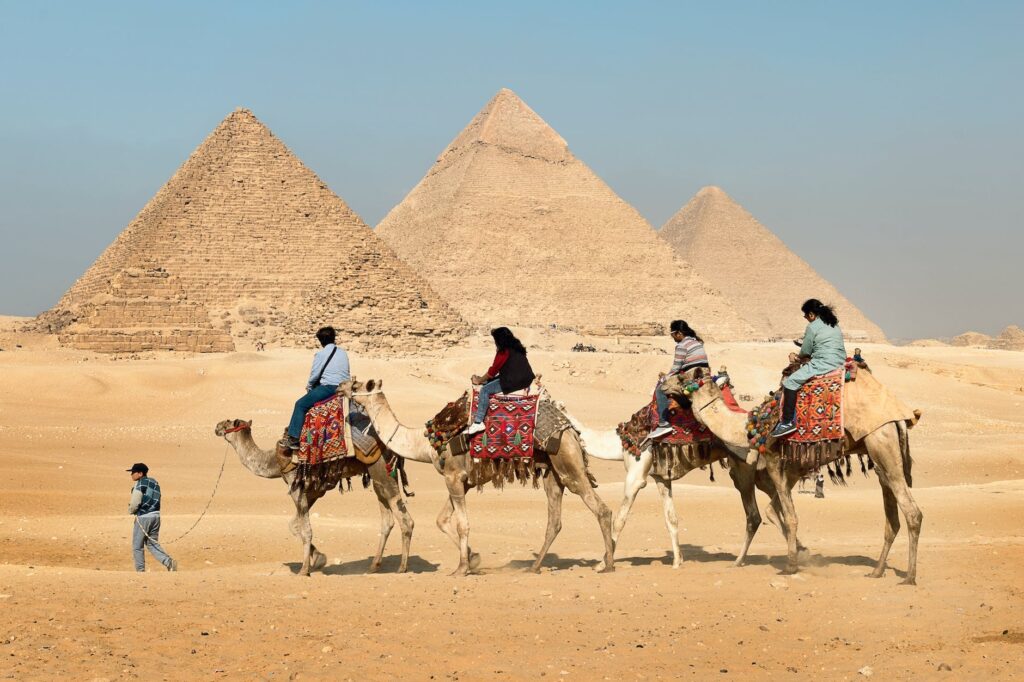 four people riding on camels across the pyramids, egypt, cairo, new cairo, egypt travel, ancient egypt, holiday and vacation to egypt, luxury travel, pyramids